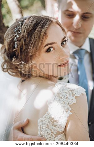 Beautiful Gorgeous Bride And Groom Posing In Sunny Spring Park Among Green Leaves. Happy Wedding Cou