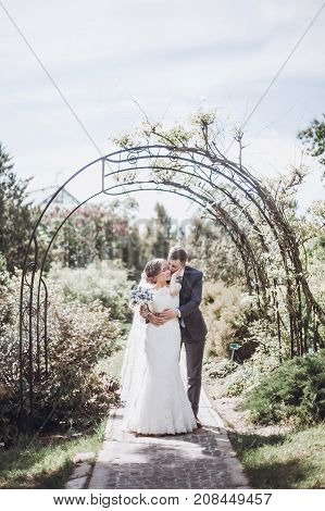 Beautiful Gorgeous Bride And Groom Posing In Sunny Spring Park Among Green Leaves. Happy Wedding Cou