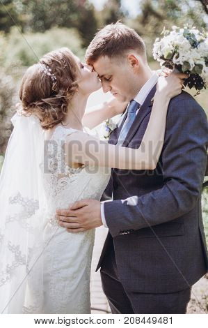 Beautiful Gorgeous Bride And Groom Kissing In Sunny Spring Park And Enjoying Day. Happy Wedding Coup