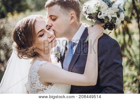 Beautiful Gorgeous Bride And Groom Kissing In Sunny Spring Park And Enjoying Day. Happy Wedding Coup