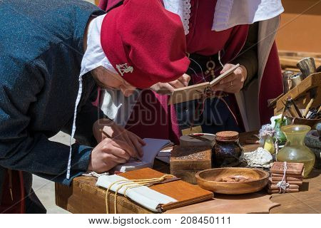 Medieval reenactors in scribe costumes practicing traditional illumination writing calligraphy with feather quill and ink, Mdina, Malta, April 2017