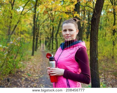 Beautiful fitness sport girl in sportswear with sports water bottle or isotonic drink in hand in autumn forest