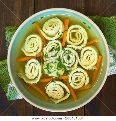 Traditional German Flaedlesuppe and Austrian Frittatensuppe based on consomme with rolls or stripes of pancake or crepe garnished with chives photographed overhead on wood with natural light (Selective Focus Focus on the soup)