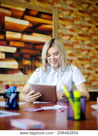 Young blond woman leaning on desk while working on her tablet with documents. Close-up. Work in the office.