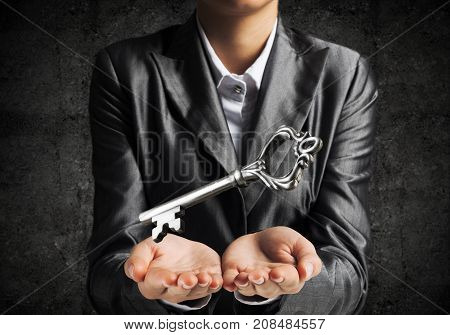 Cropped image of businessman in suit keeping big key in hands with dark wall on background.
