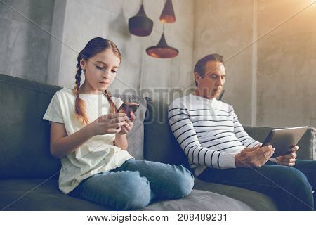 Tech living. Low angle shot of a mature parent and his preteen child sitting separately on a sofa and ignoring each other while playing games on their gadgets at home.