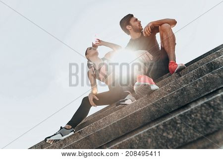 Refreshing after training. Young couple in sport clothing having a pause to drink water while sitting on the stairs outdoors