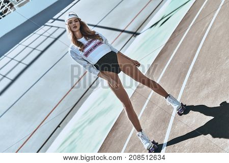 Seductive young female. Full length of attractive young and trendy woman in roller skates standing on stadium outdoors