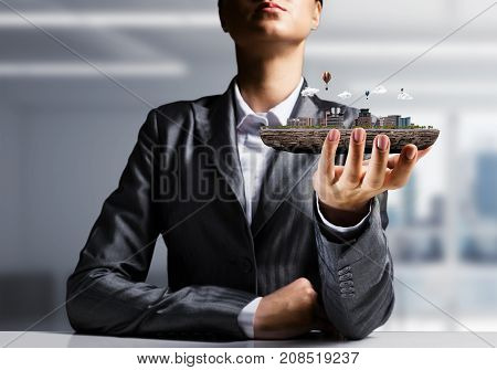 Cropped image of businessman in suit presenting in his hand modern city block with office view on background. 3D rendering.
