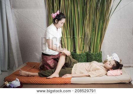Thai Masseuse doing massage for woman in spa salon. Asian beautiful woman getting thai herbal massage compress massage in spa.She is very relaxed. Healthy Concept