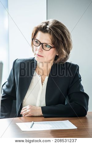 Mature business woman in flasses sitting at meeting table in office