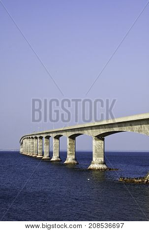 Vertical of the Confederation Bridge winding across to Prince Edward Island with seagulls on large rocks at the bridge's base on a sunny afternoon in August.