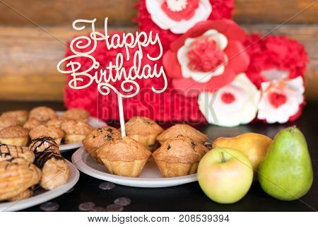 Birthday cakes and muffins with wooden greeting sign on rustic background. Wooden sing with letters Happy Birthday and holiday sweets