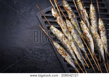 Traditional Spanish barbecue sardines on a wooden skewer as top view on a grillage 