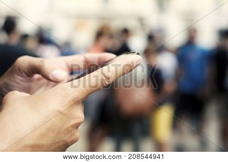 closeup of a young caucasian man using a smartphone in the street, with unrecognizable people in the background