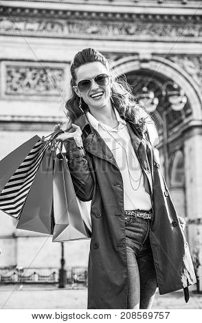 Stylish autumn in Paris. Portrait of smiling young fashion-monger in trench coat with shopping bags in Paris France
