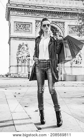 Stylish autumn in Paris. Full length portrait of elegant woman in trench coat near Arc de Triomphe in Paris France with shopping bags looking into the distance