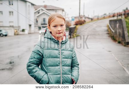 Outdoor portrait of pretty 8 year old girl on a rainy day wearing green jacket