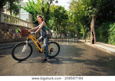 Young attractive woman riding a bicycle on wet road after rain. Sunny morning bike walk on vacation.