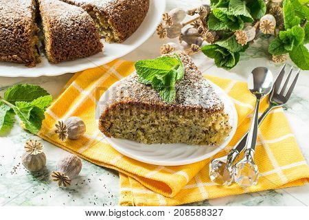 Delicious homemade poppy cake. Baking in multicooker. Whole pie and piece on yellow napkin mint and dry poppy capsule with seeds on table