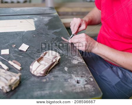 Master in a red uniform closeup of various tools collects a wooden model of a car