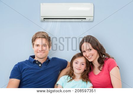 Happy Family Sitting On Sofa Under Air Conditioning At Home