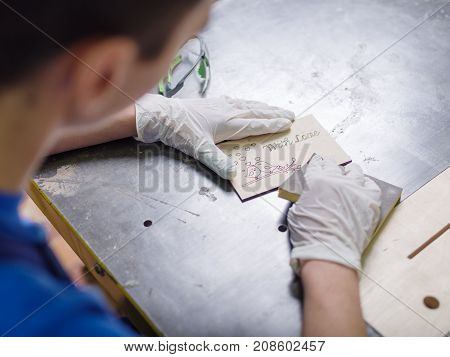 The carved plate on which the patterns and inscriptions are burned out which the master in blue overalls is stripping with a special tool