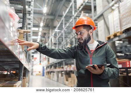 Warehouse manager checking his inventory in a large warehouse. using the tablet via the Internet is checking stock availability