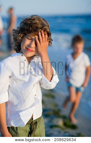 Portrait of boy of 10-11 years against the background of the rough sea. He covers eyes with a palm from the blinding sun.