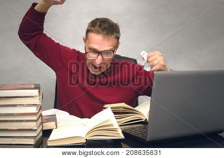Young student man becomes hysterical from studying. Office worker overworked at work. Mad student sitting at the table and throws the piece of paper and prevents to lead a lesson. Bad day.