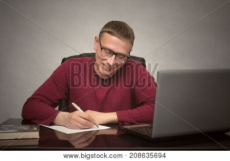 Young happy student man doing homework at the desk table. Young smiling business man signing contract or working with documents.