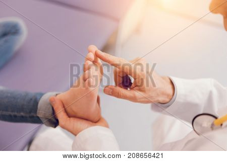 Give it me. Competent doctor sitting in semi position and holding foot while touching toe