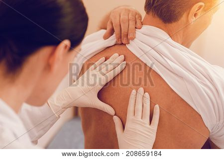 Strong body. Serious practitioner wearing rubber gloves and bowing head while doing health checkup