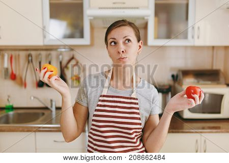 A Young Confused And Pensive Woman In An Apron Decides To Choose A Red Or Yellow Tomato In The Kitch