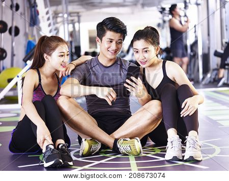 young asian man and women using mobile phone in gym while taking a break during exercising.