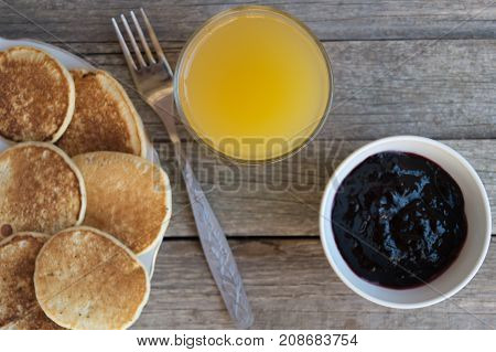 Breakfast with pancakes and orange juice with fork and blueberry jam on a wooden table