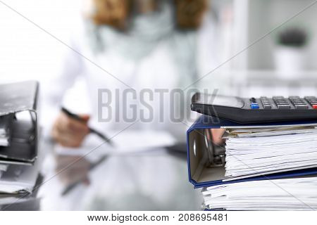 Calculator and binders with papers are waiting to be processed by businesswoman or secretary back in blur. Internal Audit and tax concept.