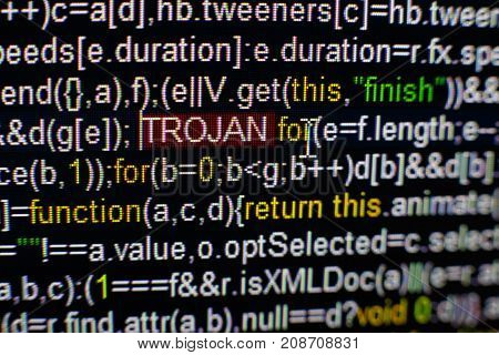 Macro photo of computer screen with program source code and highlighted TROJAN inscription in the middle. Computer script on the screen with virus in it. Cyber security concept.