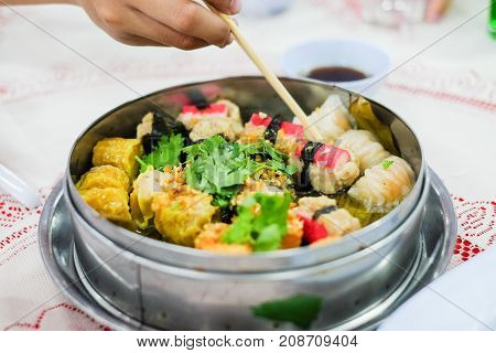 Hand holding chopsticks for eating mixed chinese steamed dumpling (dim sum) crab stick ha gow seaweed coriander and garlic for background or texture - food chinese concept.