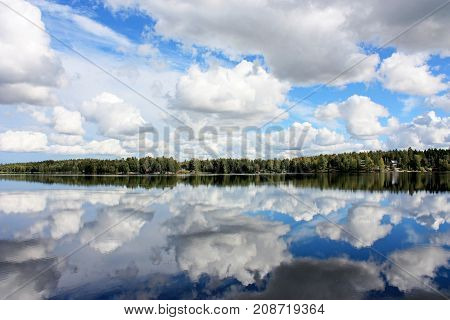Tranquil landscape at the lake with the blue sky white clouds and a forest reflected symmetrically in the clean blue water