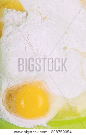 Cracked fresh eggs on white flour in green bowl reedy to be mix