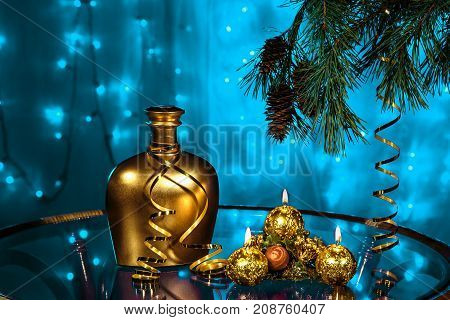 A bottle of brandy and three candles in New year and Christmas with Christmas tree branches on blurred blue background
