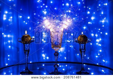 Glass with sparklers two round candles on blurred blue background