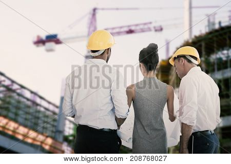 Rear view of architects discussing over blueprint against work in progress in the city