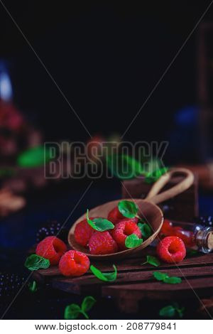 Assorted berries in a handmaiden wooden plate. Raspberry and blackberry with green mint leaves. Dark food photography with copy space.