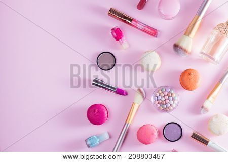Make up products and macaroons border on pink background