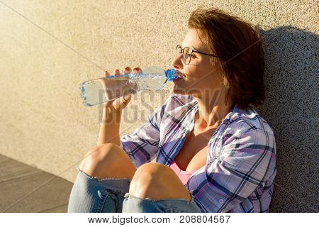 Adult healthy woman drinks water from bottle. Outdoor portrait.