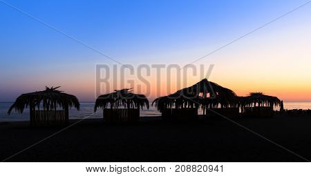 Silhouettes of hovels with the roofs covered with palm leaves for rest on the beach at sunset
