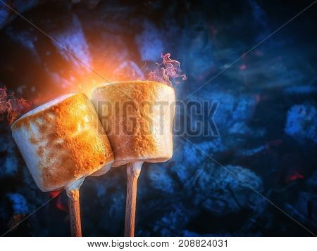 Two brown sweet marshmallows roasting over fire flames. Marshmallow on skewers roasted on charcoals. Sweet love concept.