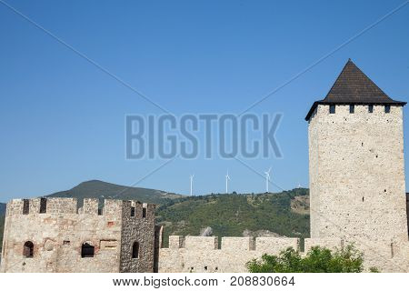 Romanian Wind Farm with Wind Turbine and windmills facing an old castle located on the Serbian side of the Danube river in the Iron Gates valley.